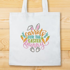 K&ouml;nnte beinhalten: Wei&szlig;e Einkaufstasche mit einem gestickten Design aus Karotten, Hasenohren und dem Text "Karotten f&uuml;r den Osterhasen".