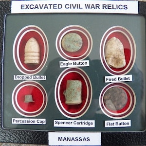 May include: A framed display of excavated Civil War relics, including a dropped bullet, a fired bullet, a percussion cap, a Spencer cartridge, an eagle button, and a flat button. The display is labeled "Excavated Civil War Relics" and "Manassas".
