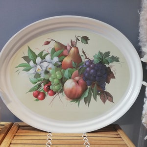 Puede incluir: Bandeja de servir ovalada blanca con un diseño pintado de frutas y flores. El diseño presenta peras, uvas, cerezas y una flor blanca con hojas verdes.
