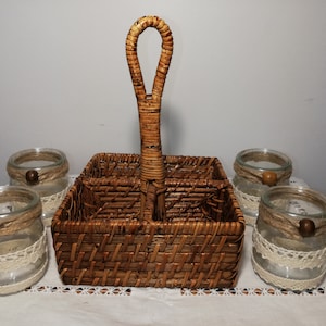 May include: A brown wicker basket with a handle, divided into four sections, holding four clear glass jars with twine and lace accents. Each jar has a small wooden bead.