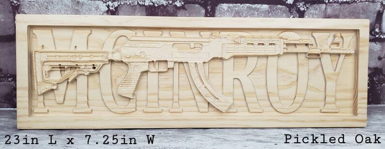 May include: A wooden sign with the name "MCINTROY" carved into it. The sign features a stylized image of a rifle with a wood grain finish. The sign is 23 inches long and 7.25 inches wide and is made of pickled oak.