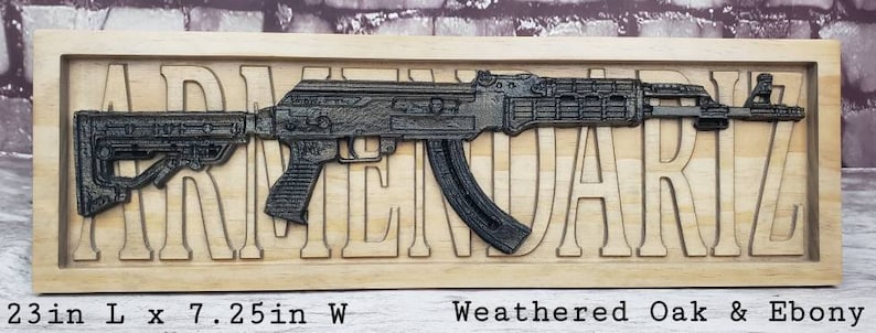 May include: A wooden sign with the word "ARMENDARIZ" carved into it. A black and silver AK-47 style rifle is mounted on the sign. The sign is 23 inches long and 7.25 inches wide. It is made of weathered oak and ebony.