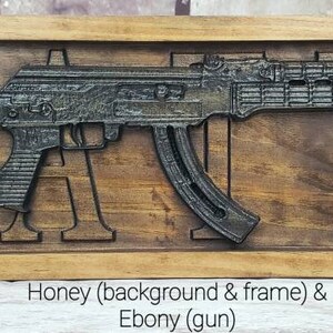May include: A wooden sign with the word "WANTS" carved into it. A black rifle is carved into the sign, with the barrel extending beyond the letters. The background and frame are honey-colored, while the gun is ebony.