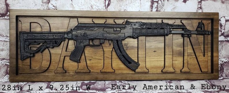 May include: A wooden sign with a black metal cutout of a rifle and the word "DAIN" carved into the wood. The sign is 28 inches long and 9.25 inches wide. It is made of Early American and Ebony wood.