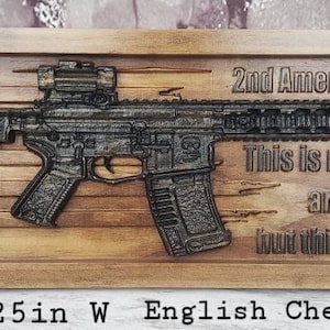 May include: A wooden sign with a carved image of a rifle and an American flag. The sign reads "2nd Amendment This is my rifle. There are many like it, but this one is mine." The sign is made of English Chestnut and Ebony wood and measures 53.3 cm long by 18.4 cm wide.