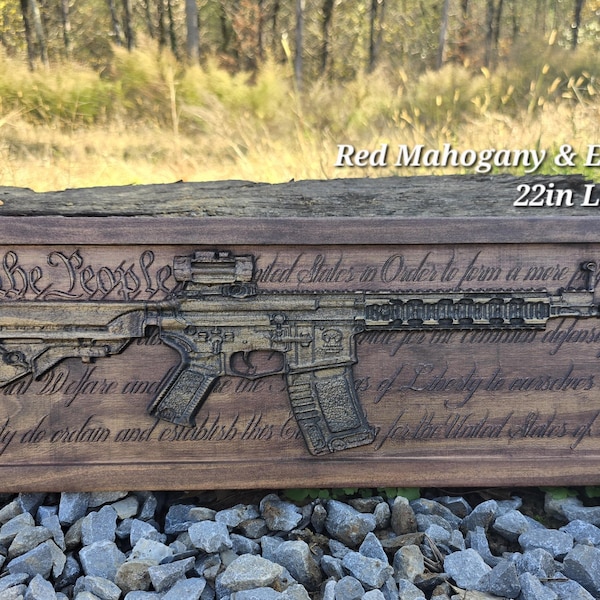 May include: A wooden plaque with a carved image of a rifle and the text "We the People of the United States, in Order to form a more perfect Union..." The plaque is stained in red mahogany and ebony. It measures 22 inches long by 7.25 inches wide.