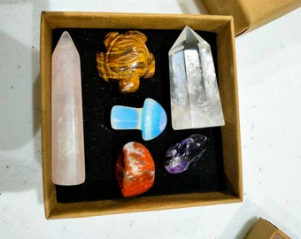 Puede incluir: Un conjunto de siete cristales pulidos en una caja marrón. Los cristales incluyen una amatista rosa, un cuarzo transparente, una tortuga de ojo de tigre, un hongo de ópalo azul, una jaspe roja y una amatista púrpura.