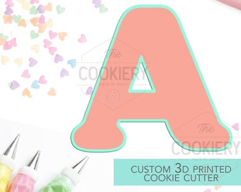 May include: A light pink 3D printed cookie cutter in the shape of the letter A. The cutter is outlined in a light turquoise color. The cutter is surrounded by colorful heart sprinkles and piping bags.
