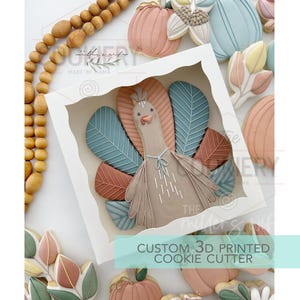 May include: A 3D printed cookie cutter in the shape of a turkey with brown, orange, and blue feathers. The cookie cutter is displayed in a white box with the text "Custom 3D Printed Cookie Cutter".