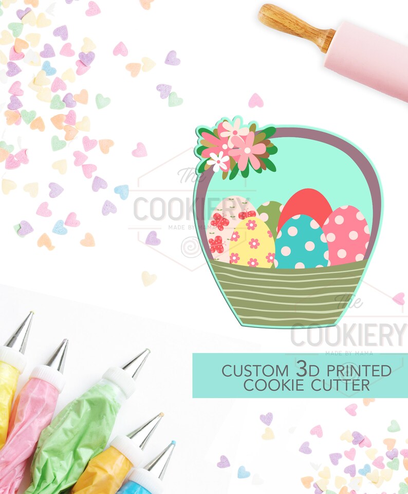 May include: A 3D printed cookie cutter shaped like a basket filled with Easter eggs. The basket is decorated with flowers and the eggs are decorated with polka dots and floral patterns. The cookie cutter is made by The Cookiery.