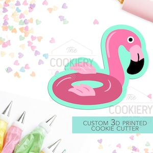 Könnte beinhalten: Ein türkisfarbener 3D-gedruckter Ausstecher in Form eines rosa Flamingos, der auf einem rosa aufblasbaren Ring schwimmt. Der Ausstecher befindet sich auf einem weißen Hintergrund mit bunten Herzstreuseln.