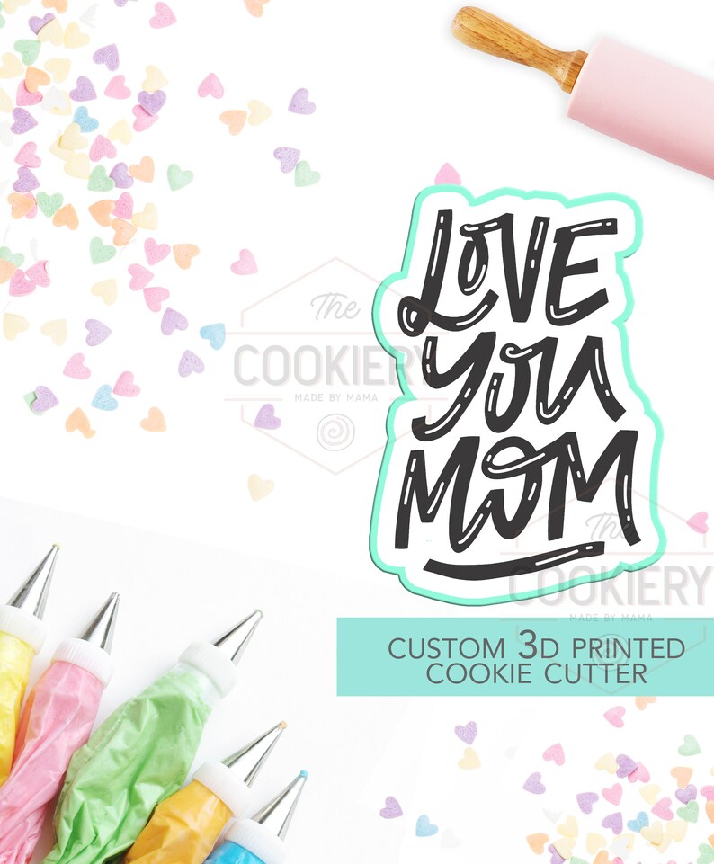 May include: A turquoise blue 3D printed cookie cutter with the words "Love You Mom" in black script font. The cutter is on a white background with colorful heart sprinkles and piping bags.