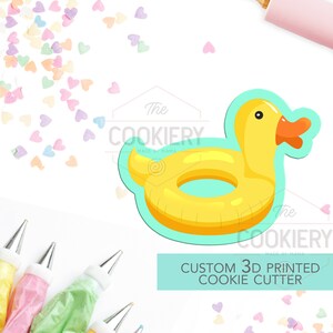 May include: A yellow rubber ducky shaped cookie cutter with a turquoise inner ring. The cutter is on a white background with colourful heart sprinkles. The text "The Cookiery Made by Mama" and "Custom 3D Printed Cookie Cutter" is also visible.