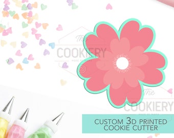 May include: A pink flower-shaped 3D printed cookie cutter with a light blue outline. The cutter is on a white background with colorful heart sprinkles. The text "CUSTOM 3D PRINTED COOKIE CUTTER" is in a light blue box.