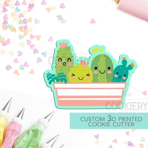 Könnte beinhalten: Ein 3D-gedruckter Ausstecher in Form eines Kaktus-Topfes mit lächelnden Gesichtern. Der Ausstecher ist rosa und weiß mit grünen Kakteen und gelben Blüten. Der Text "CUSTOM 3D PRINTED COOKIE CUTTER" befindet sich auf einem türkisfarbenen Hintergrund.