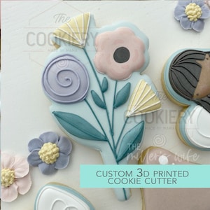 May include: A 3D printed cookie cutter in the shape of a bouquet of flowers. The flowers are pink, purple, and yellow. The leaves are green. The cookie cutter is on a white background. The text "CUSTOM 3D PRINTED COOKIE CUTTER" is printed on the background.