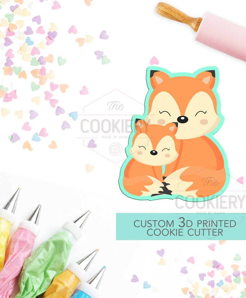 K&ouml;nnte beinhalten: Ein 3D-gedruckter Ausstecher in Form einer Mutter und eines Babyfuchses. Der Ausstecher ist orange mit hellblauen Konturen. Das Bild enth&auml;lt auch eine Teigrolle, Spritzbeutel und herzf&ouml;rmige Streusel. Der Text auf dem Bild lautet "CUSTOM 3D PRINTED COOKIE CUTTER".