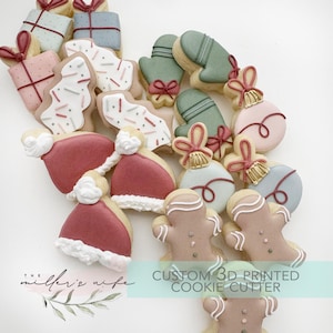 Könnte beinhalten: Eine Sammlung von Weihnachtsplätzchen, darunter Geschenkboxen, Fäustlinge, Ornamente, Lebkuchenmänner und Weihnachtsmützen. Die Kekse sind mit verschiedenen Farben und Designs verziert, darunter rote, weiße und grüne Glasur. Der Text "CUSTOM 3D PRINTED COOKIE CUTTER" ist sichtbar.