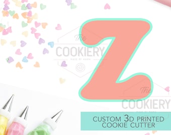 May include: A custom 3D printed cookie cutter in the shape of the letter Z. The cutter is light pink with a turquoise outline. The cutter is surrounded by colorful heart sprinkles and piping bags.
