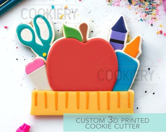 May include: A 3D printed cookie cutter shaped like a red apple with a green leaf, a ruler, a pair of scissors, a crayon, and a glue stick. The cookie cutter is labeled "Custom 3D Printed Cookie Cutter".