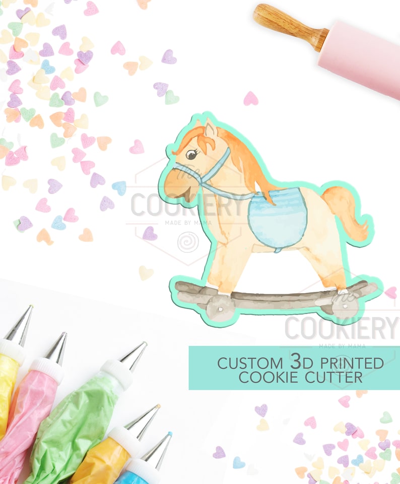 May include: A 3D printed cookie cutter shaped like a rocking horse. The horse is light brown with a blue saddle and a light brown mane. The cookie cutter is on a white background with colorful sprinkles.