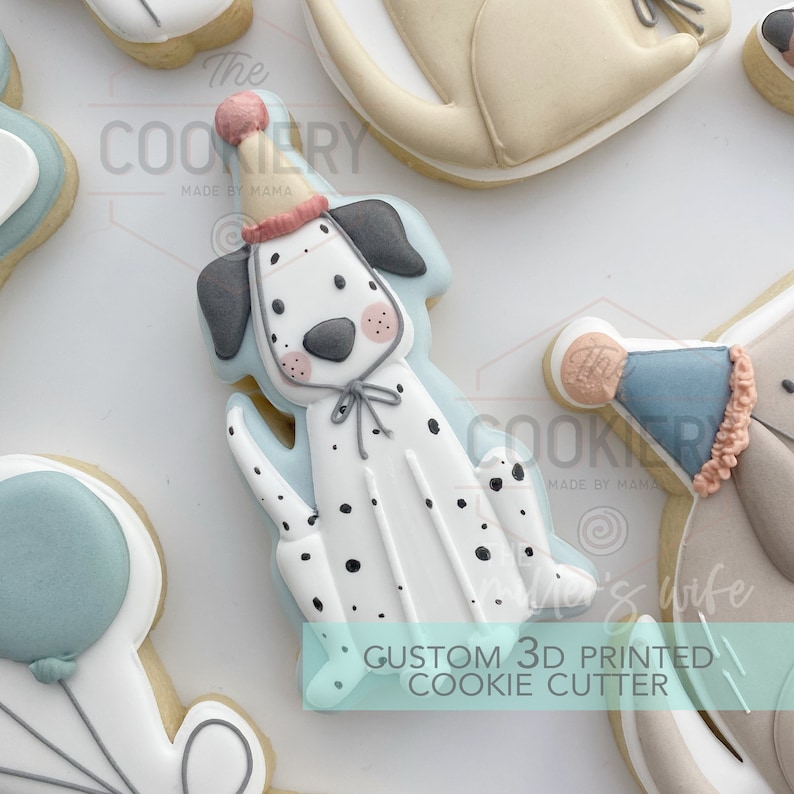 May include: A white and black Dalmatian dog cookie cutter with a blue and pink party hat. The cookie cutter is 3D printed and says "Custom 3D Printed Cookie Cutter" on the bottom.