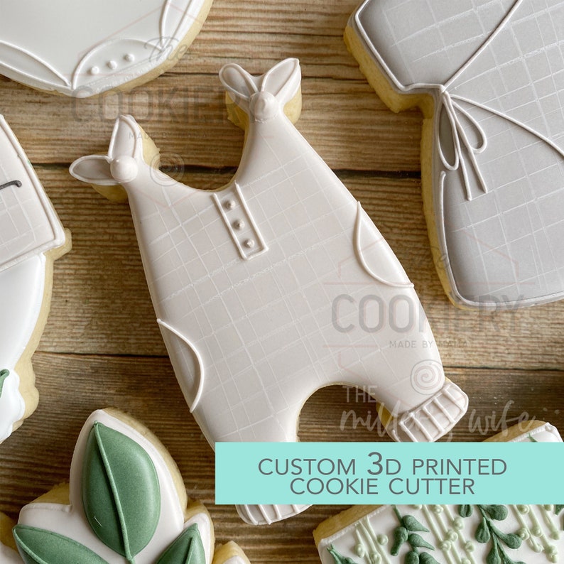 May include: A white 3D printed cookie cutter shaped like a baby onesie. The onesie has a grid pattern and buttons. The text "CUSTOM 3D PRINTED COOKIE CUTTER" is on a blue background.