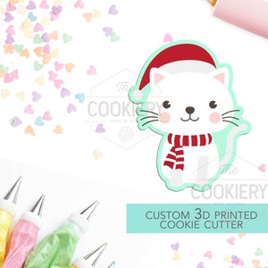 May include: A white cat wearing a red Santa hat and a red and white striped scarf. The cat is a 3D printed cookie cutter. The text "CUSTOM 3D PRINTED COOKIE CUTTER" is on a light blue background.