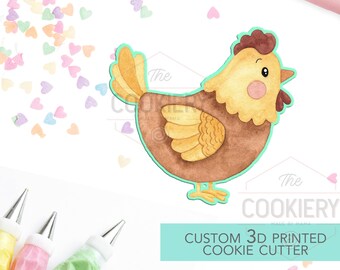 May include: A brown and yellow 3D printed cookie cutter shaped like a cartoon chicken. The cutter is on a white background with colourful heart sprinkles and piping bags.