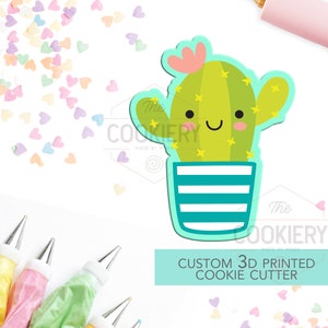 Könnte beinhalten: Ein grüner Kaktus-Ausstecher mit einem lächelnden Gesicht, einer rosa Blume und gelben Sternen. Der Kaktus befindet sich in einem blau-weiß gestreiften Topf. Der Ausstecher ist 3D-gedruckt und ein individuelles Design. Der Text "CUSTOM 3D PRINTED COOKIE CUTTER" befindet sich auf einem hellblauen Hintergrund.