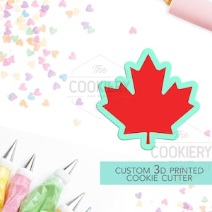 May include: Red 3D printed cookie cutter shaped like a Canadian maple leaf. The cutter is on a white surface with colorful heart sprinkles. The text "CUSTOM 3D PRINTED COOKIE CUTTER" is on a turquoise background.