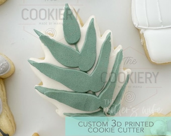 May include: A 3D printed cookie cutter in the shape of a green leafy branch. The cutter is on a white background with the text "The Cookiery Made by Mama" and "Custom 3D Printed Cookie Cutter".
