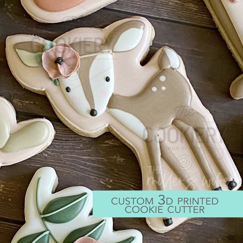 May include: A 3D printed cookie cutter in the shape of a brown deer with white spots. The deer is wearing a pink flower headband. The text "CUSTOM 3D PRINTED COOKIE CUTTER" is on a turquoise background.