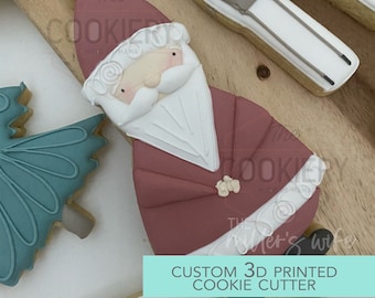 Könnte beinhalten: Ein 3D-gedruckter Ausstecher in Form des Weihnachtsmanns. Der Ausstecher ist aus weißem Kunststoff und hat ein rotes und weißes Design. Der Text "CUSTOM 3D PRINTED COOKIE CUTTER" ist auf einem türkisfarbenen Hintergrund gedruckt.