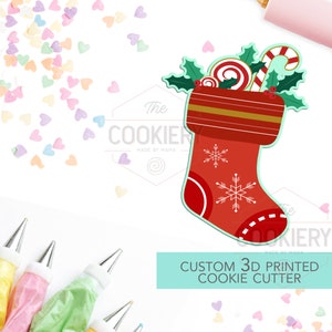 May include: Red and white Christmas stocking cookie cutter with candy canes, holly, and a snowflake design. The cutter is 3D printed and says "The Cookiery Made by Mama" on the bottom.  Custom 3D Printed Cookie Cutter.