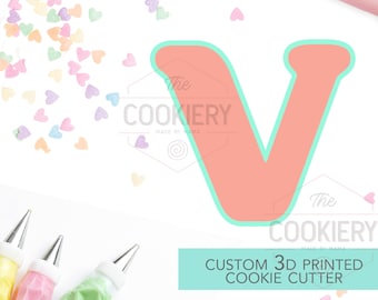 May include: A light pink 3D printed cookie cutter in the shape of the letter V. The cutter is surrounded by pastel pink, yellow, and blue heart sprinkles. The text "CUSTOM 3D PRINTED COOKIE CUTTER" is written in white on a light blue background.