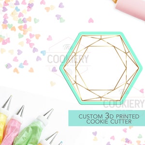 Puede incluir: Un cortador de galletas impreso en 3D de color azul turquesa con forma de diamante geométrico con líneas doradas. El cortador está sobre un fondo blanco con chispas de corazón de color rosa pastel, amarillo y azul. El texto "CUSTOM 3D PRINTED COOKIE CUTTER" está escrito en blanco sobre un fondo azul turquesa.