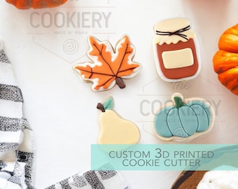 May include: Set of five 3D printed cookie cutters in fall themes. The cutters are for a pear, a leaf, a jar, a pumpkin, and a pumpkin with a stem. The cutters are made of white plastic and are shown on a white surface.