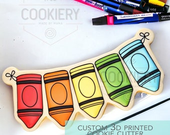 Op de afbeelding: Een 3D-geprinte koekjesvormer in de vorm van een banner van vijf kleurpotloden. De kleurpotloden zijn rood, oranje, geel, groen en blauw. De koekjesvormer is gelabeld "CUSTOM 3D PRINTED COOKIE CUTTER".
