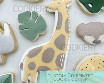 Könnte beinhalten: Ein 3D-gedruckter Ausstecher in Form einer Giraffe. Die Giraffe ist gelb mit braunen Flecken und hat einen langen Hals mit einer Krone auf dem Kopf. Der Ausstecher befindet sich auf einem weißen Hintergrund mit anderen Ausstechern im Hintergrund. Der Text "CUSTOM 3D PRINTED COOKIE CUTTER" befindet sich am unteren Rand des Bildes.