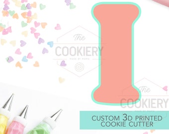 May include: A light pink 3D printed cookie cutter in the shape of the letter I. The cutter is on a white background with colorful heart sprinkles and piping bags.