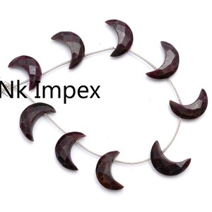 May include: A strand of dark red gemstone crescent moon beads on a silver chain with white tassels.  Nk Impex.