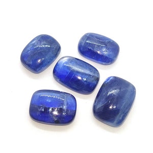 May include: Five blue kyanite gemstone cabochons, each with a rectangular shape and a smooth, polished surface. The stones have a deep blue color with a slight shimmer.