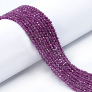 May include: A strand of deep purple faceted gemstone beads. The beads are small and round, and they are strung on a clear thread.