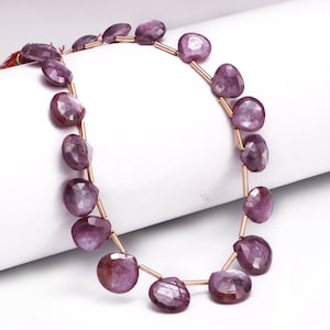 May include: A strand of purple gemstone beads with a faceted, teardrop shape. The beads are strung on a thin gold wire.