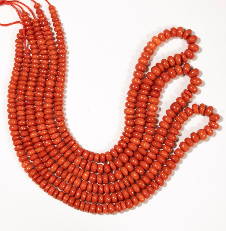May include: A strand of bright orange coral beads. The beads are round and smooth, and they are strung on a thin cord. The coral beads are arranged in a loose, flowing pattern.