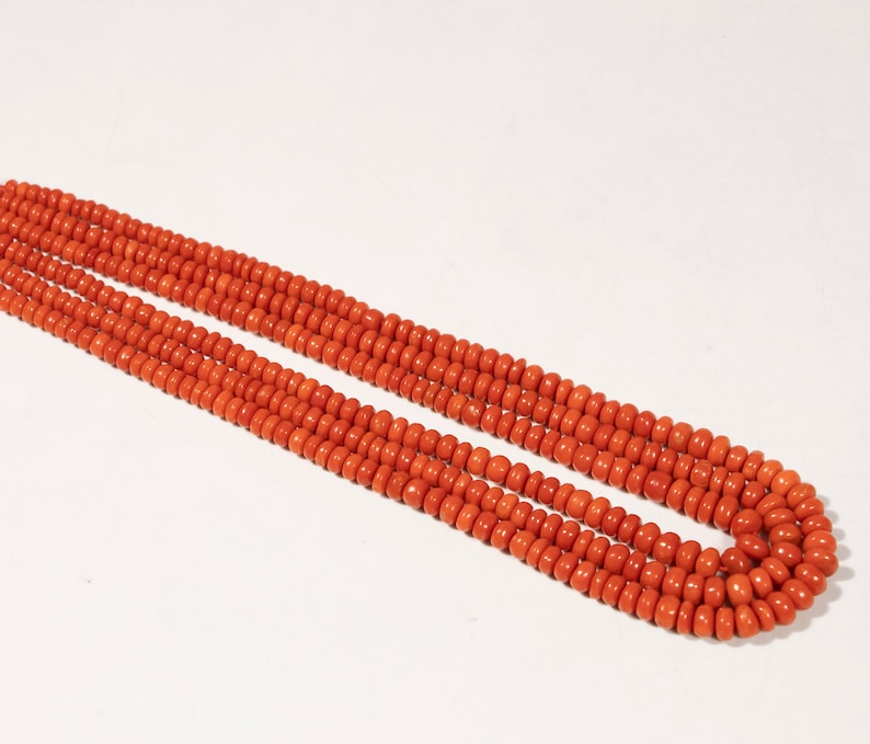 May include: A long strand of bright orange coral beads. The beads are round and uniform in size, creating a smooth and continuous line.