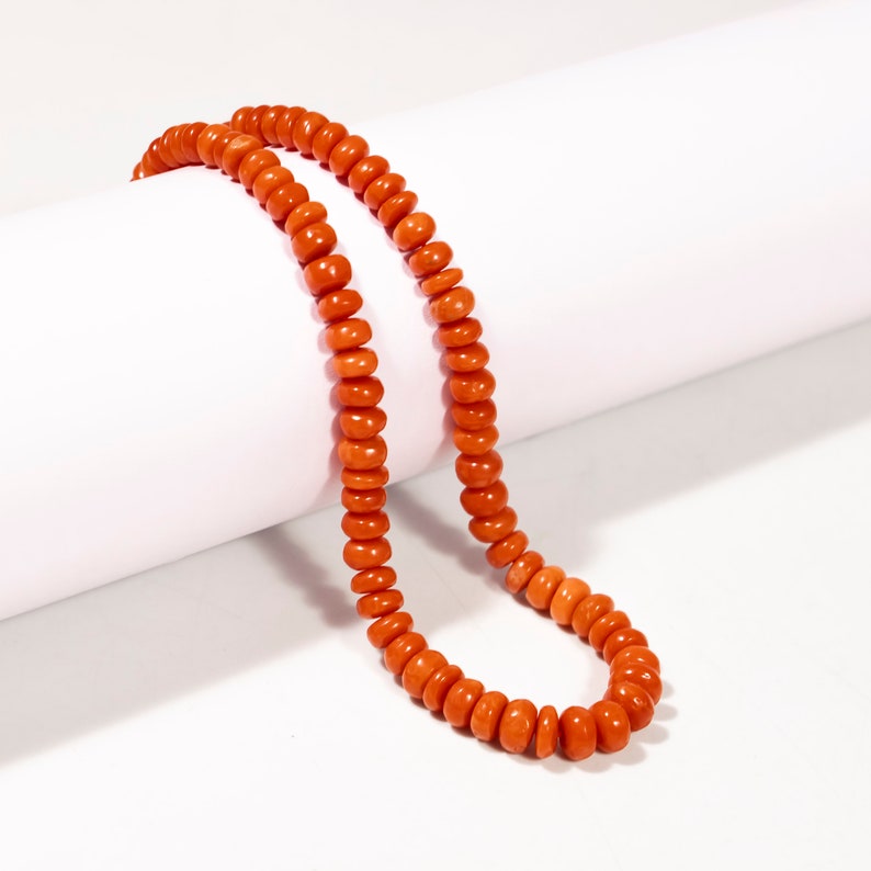 May include: A long strand of orange coral beads, strung together to form a necklace.