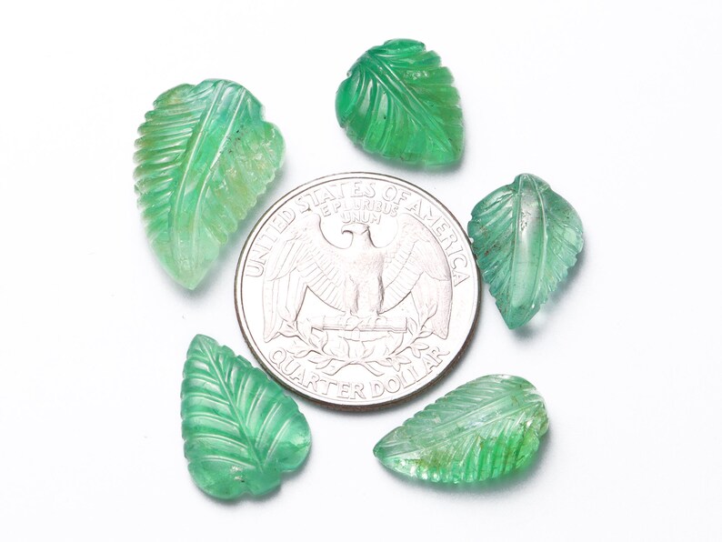 May include: Five green gemstone leaf-shaped beads, each with a carved vein pattern, are arranged in a circle around a US quarter dollar coin. The beads are approximately the size of the coin.