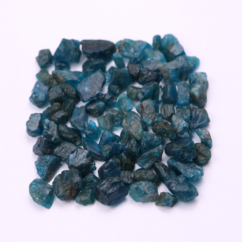 May include: A collection of blue-green gemstone chips. The chips are rough and have a variety of shapes and sizes.